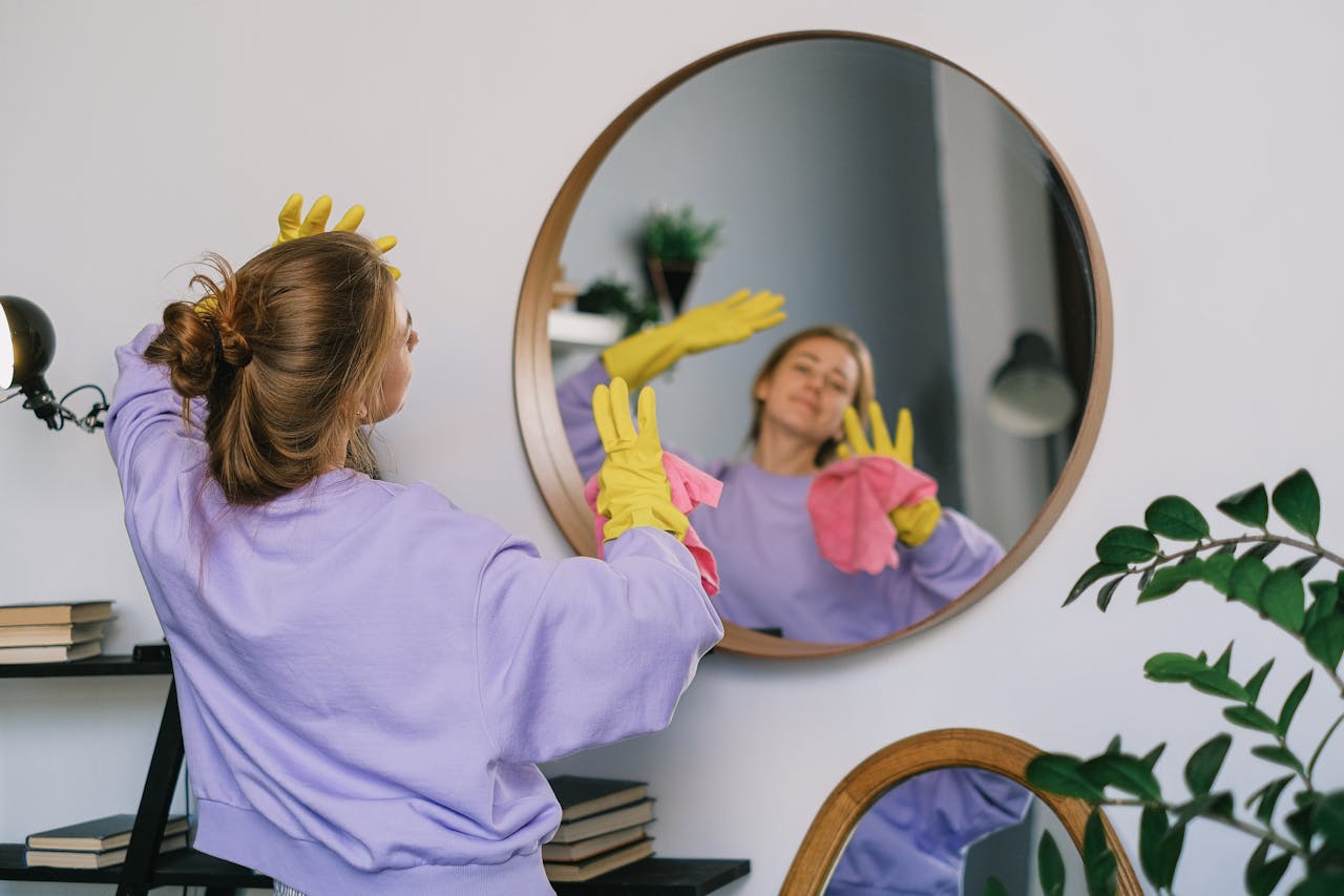 hero-01 Back view of young female in casual clothes and latex gloves standing against mirror and dancing while cleaning light room in daytime